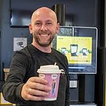 Coffee cup held by smiling man at tech store or office environment.